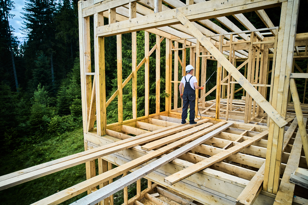 Worker applying fire-retardant to composite wood during outdoor deck installation near forest.
