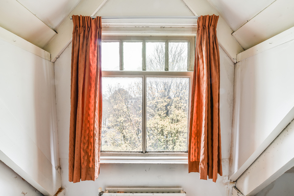 Attic space showcasing traditional casement window framed by orange curtains