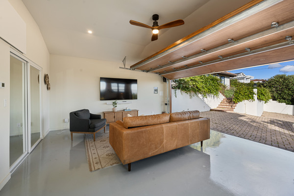 Cozy garage conversion with couch, TV, ceiling fan, and open garage door for indoor-outdoor living