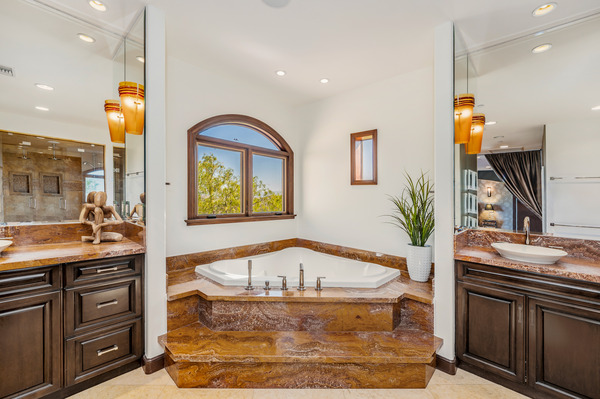 Elegant jacuzzi tub in a luxury master bathroom featuring dark wood cabinetry and dual sinks