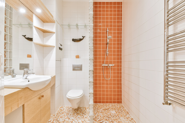 Small bathroom with orange shower tiles and wall-mounted sink, demonstrating tiled shower ideas and bathroom