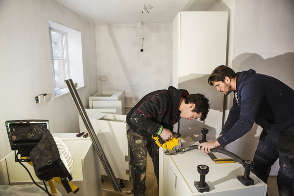 remodeling home service – local home building contractors near me preparing kitchen space Two builders measuring and cutting materials for remodeling home service provided by local home building contractors near me