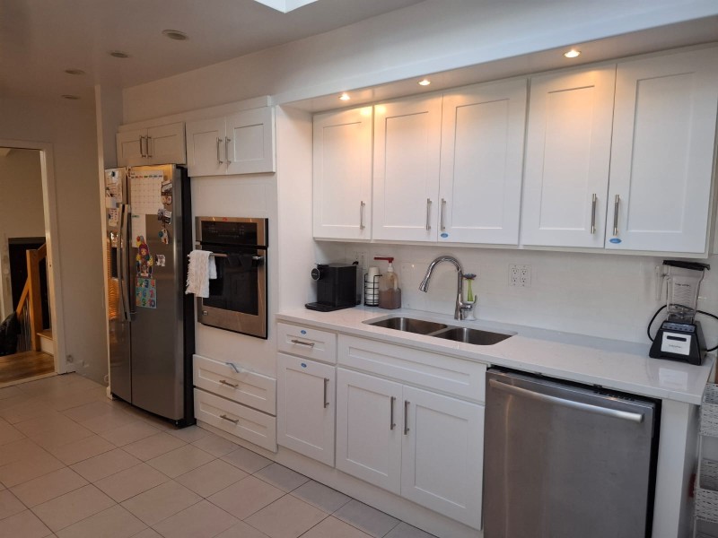 Professional kitchen remodel featuring white shaker cabinets, quartz countertops, stainless steel appliances, built-in wall oven, undermount sink, and under cabinet lighting with skylight